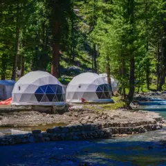 Dome-shaped namioty w lesie nad rzeką to przykład, co to jest glamping. Luksusowy wypoczynek na łonie natury.