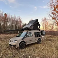 Zmodyfikowany caddy kamper z namiotem dachowym i panelem słonecznym gotowy na przygodę w lesie.