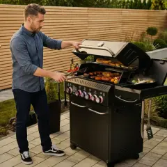 Mężczyzna przygotowuje kiełbaski i bułki na grillu. Warto mieć pod ręką wszystko, co zabrać na grilla, by cieszyć się smacznym posiłkiem w ogrodzie.