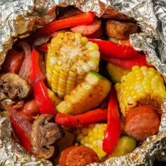 Pyszne sakiewki na grilla z kukurydzą, papryką, pieczarkami i kiełbasą, zapakowane w folię aluminiową.