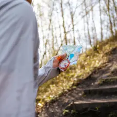 Osoba trzyma mapę i kompas, ucząc się, jak wyznaczyć azymut w lesie.