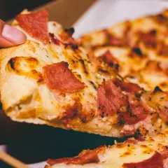 Palce sięgają po kawałek pysznej pizzy na kamieniu, z ciągnącym się serem i kawałkami wędliny.