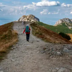 Szlak na czerwone wierchy z Kuźnic. Turystka z plecakiem idzie kamienistą ścieżką wśród traw.