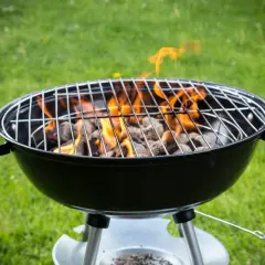 Rozpalony grill węglowy z płomieniami na trawie. Idealny do nauki, jak rozpalic grilla na letnie wieczory.