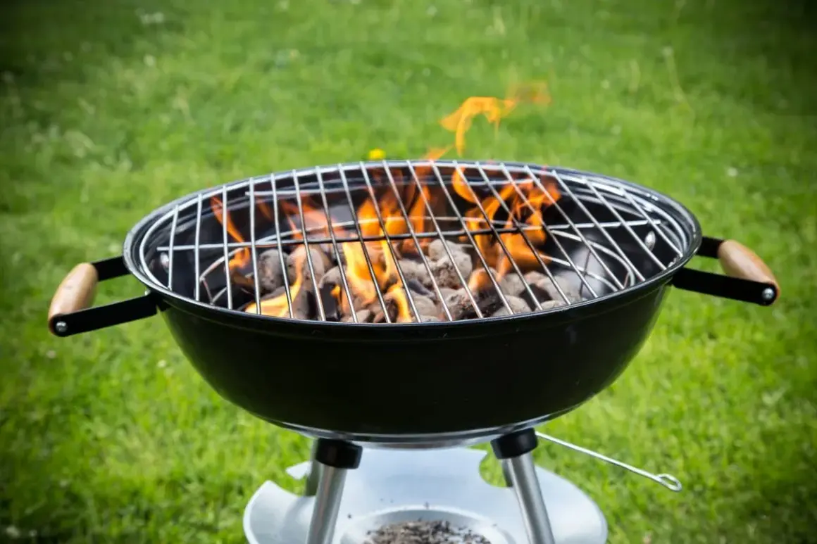 Rozpalony grill węglowy z płomieniami na trawie. Idealny do nauki, jak rozpalic grilla na letnie wieczory.
