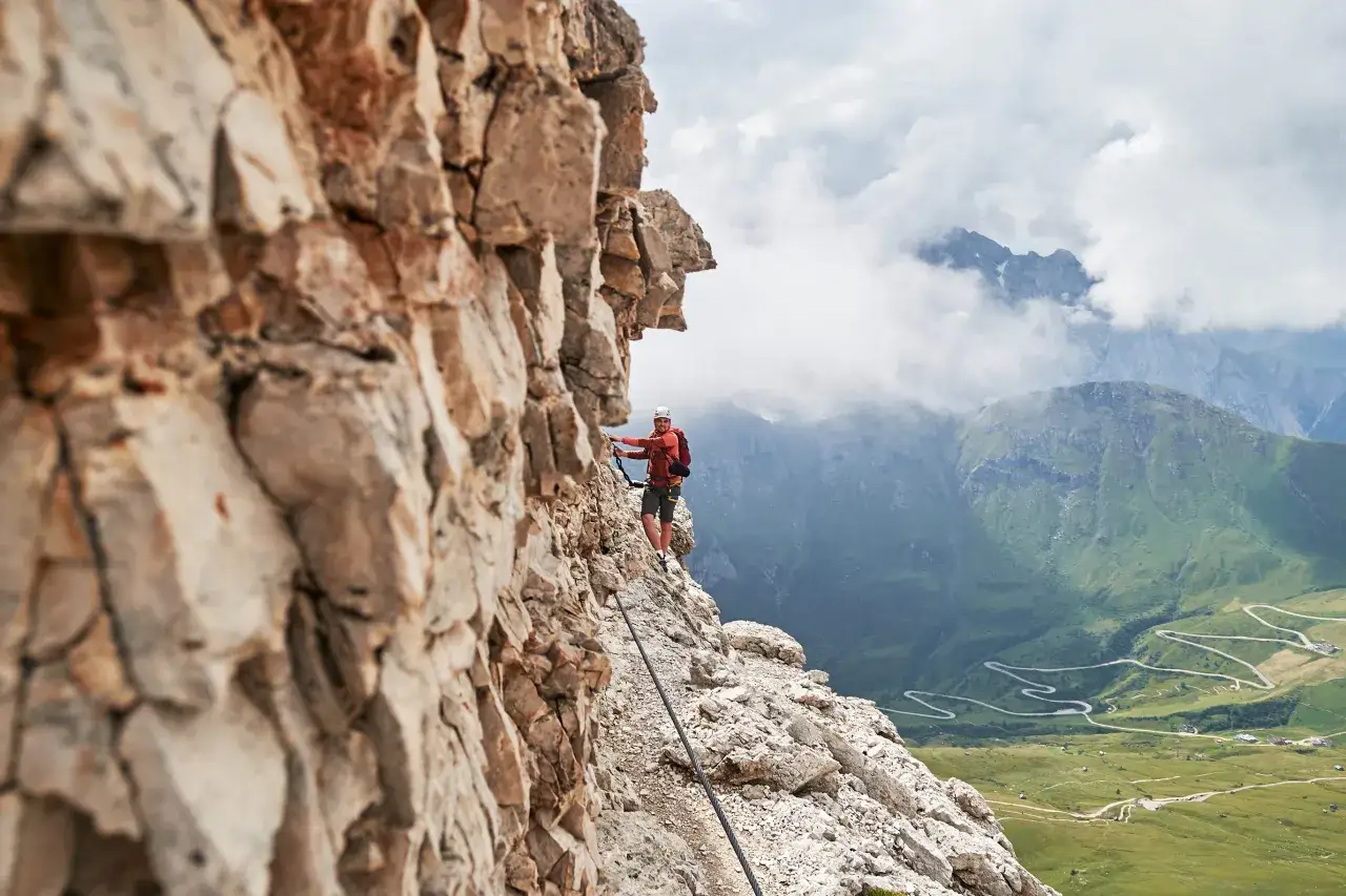 Wspinacz na ferratach w Dolomitach, z widokiem na kręte drogi i zielone doliny.