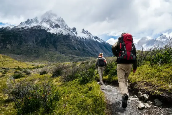 Trekking co to? Dwóch turystów z plecakami wędruje szlakiem w górach. Majestatyczne, ośnieżone szczyty w tle.