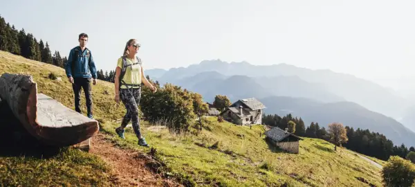 Para idzie na trekking po górach. W tle widać chatki i pasma górskie.
