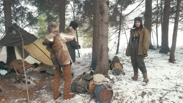 Oto przykład, bushcraft co to: ludzie w zimowym lesie, namiot, futrzane okrycie, plecaki.
