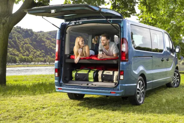 Para relaksuje się w kamperze Opel Vivaro, z widokiem na rzekę i kemping.
