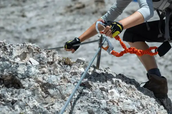 Ręce w rękawiczkach pewnie trzymają linę na via ferrata dla początkujących. Karabińczyk i lonża zapewniają bezpieczeństwo podczas wspinaczki.