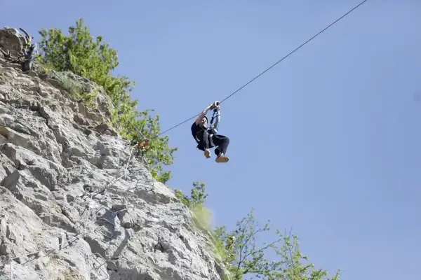 Człowiek zjeżdża na tyrolce obok skalnej ściany z ubezpieczeniami, jak na via ferrata polska.