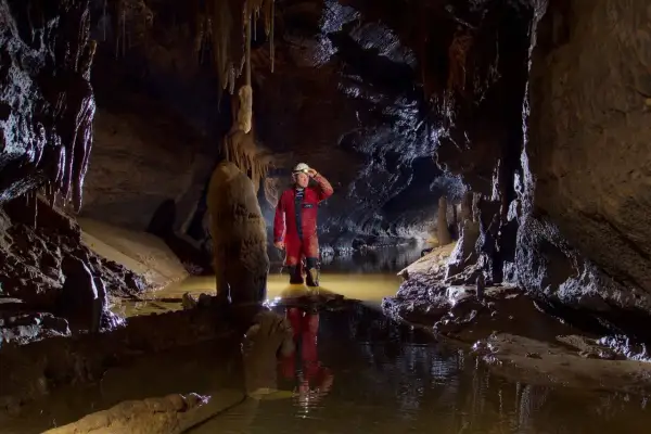 Odkrywca w jaskini, zanurzony po kolana w wodzie, bada podziemny świat. To właśnie jest speleologia – fascynująca podróż w głąb Ziemi.