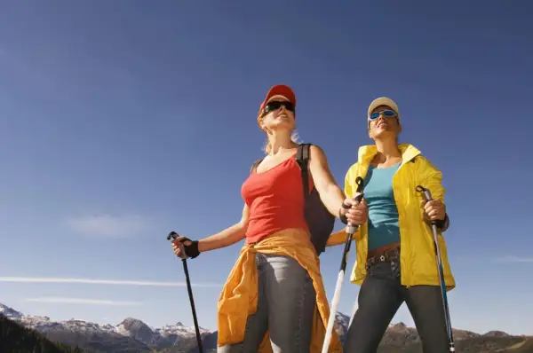Dwie kobiety z kijkami do nordic walking podziwiają górski krajobraz.
