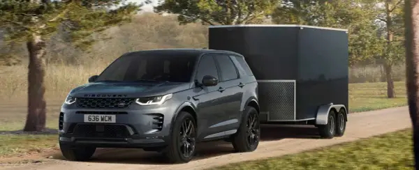 Szary Land Rover Discovery Sport z przyczepą kempingową na leśnej drodze. Idealny samochód do przyczepy kempingowej.